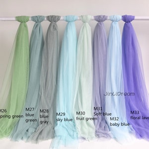 May include: Nine different colors of tulle fabric swatches, hanging from a white rod. The colors are spring green, blue green, blue gray, sky blue, fruit green, soft blue, baby blue, and floral lavender.
