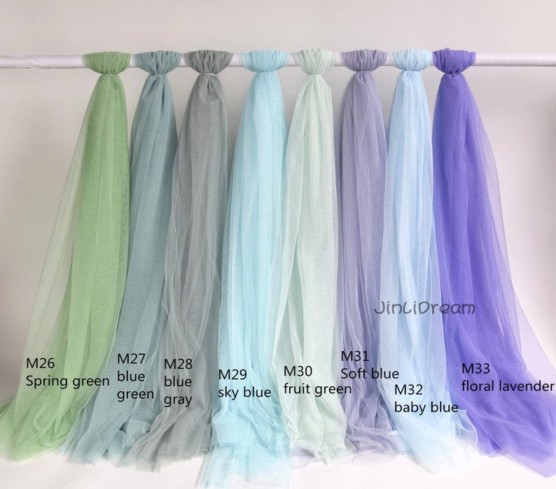 May include: Nine different colors of tulle fabric swatches, hanging from a white rod. The colors are spring green, blue green, blue gray, sky blue, fruit green, soft blue, baby blue, and floral lavender.