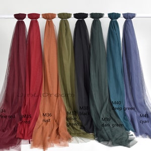 May include: Assortment of ten sheer fabric swatches in various colors, including wine red, red, rust, olive green, black, dark green, deep green, and cyan. The swatches are hung on a white rod.