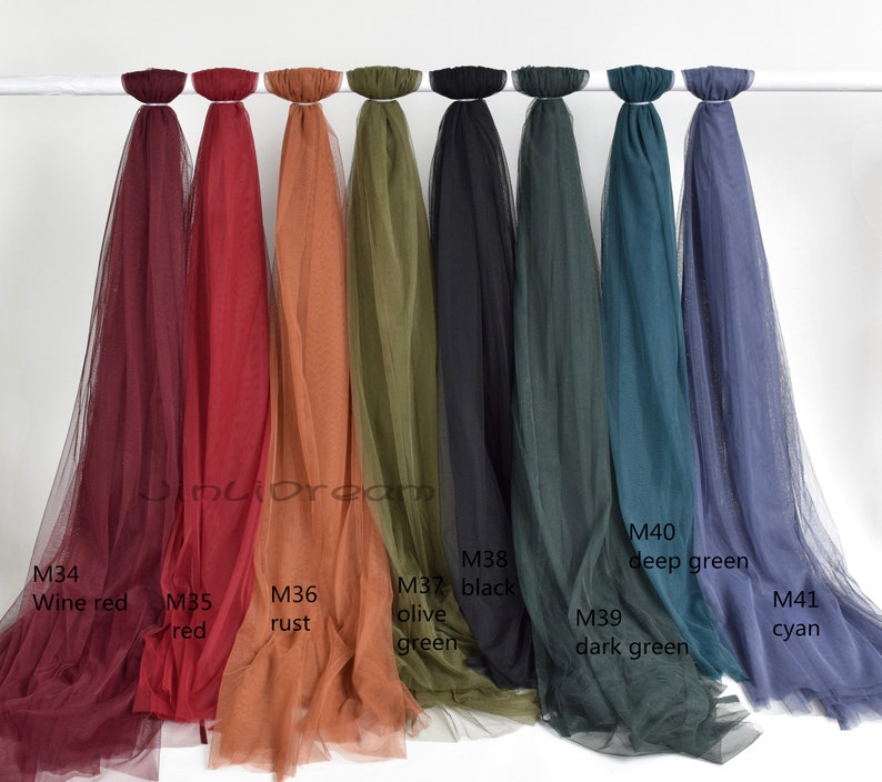 May include: Assortment of ten sheer fabric swatches in various colors, including wine red, red, rust, olive green, black, dark green, deep green, and cyan. The swatches are hung on a white rod.
