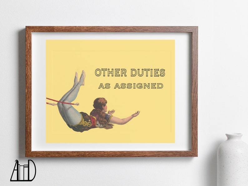 May include: Framed print featuring a vintage illustration of a woman in a circus act, mid-air. The text "OTHER DUTIES AS ASSIGNED" is displayed in black. The artwork is set against a yellow background, framed in a brown wooden frame.