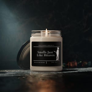 May include: A white candle in a glass jar with a black label that reads "Smells Just Like Heaven" and "100% Soy Wax Blend". The candle is lit and the flame is visible.