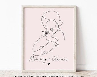 May include: A framed art print featuring a minimalist line drawing of a mother holding a baby. The artwork is in black on a pink background, with the text "Mommy & Olivia" and a heart symbol. The frame is light-colored.