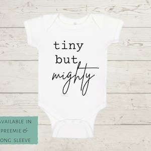 May include: White baby onesie with black text that reads "tiny but mighty".