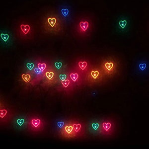 May include: A dark background with multiple colorful heart-shaped lights. The lights are in various colors, including red, orange, yellow, green, blue, and purple.