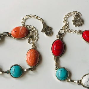 May include: Two bracelets with turquoise, red, and orange oval stones and silver chain links. One bracelet has a charm that says "Made with an Angel".