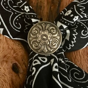 May include: A silver-toned metal bandana clasp with a floral design. The clasp is attached to a black and white bandana.