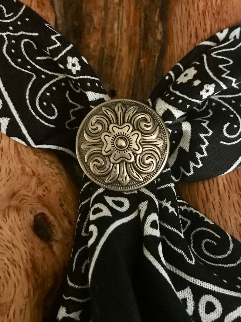 May include: A silver-toned metal bandana clasp with a floral design. The clasp is attached to a black and white bandana.