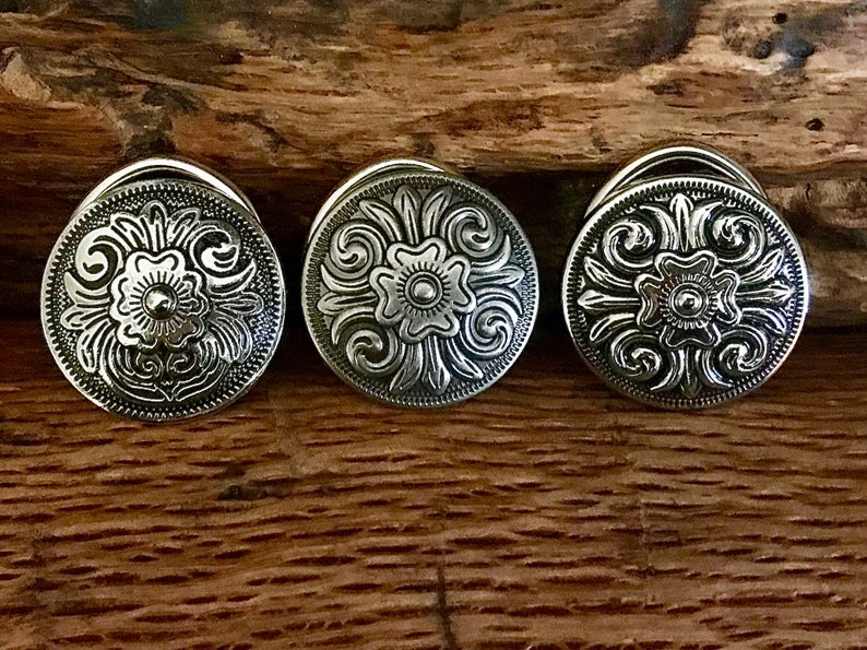 May include: Three silver-toned metal buttons with a floral design. The buttons are round and have a raised design.