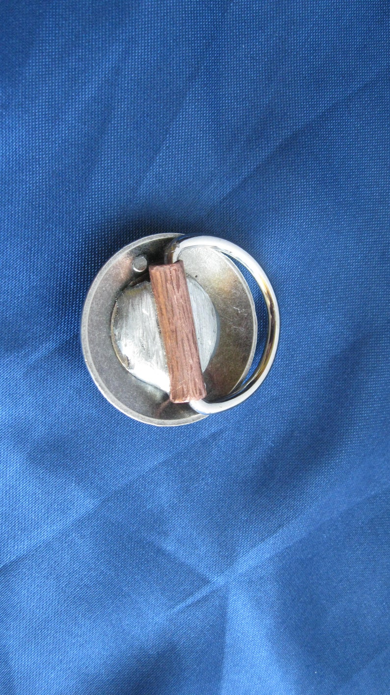 May include: A silver metal belt buckle with a wooden insert. The buckle has a rounded shape and a ring for attaching a belt.