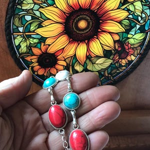 May include: A silver chain bracelet with turquoise and red oval-shaped stones. The bracelet is on a hand against a background of a stained glass sunflower.