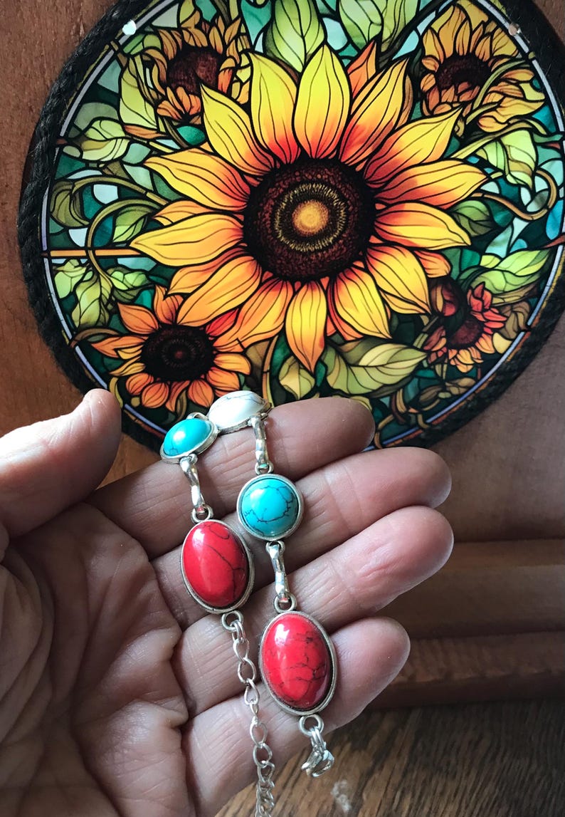 May include: A silver chain bracelet with turquoise and red oval-shaped stones. The bracelet is on a hand against a background of a stained glass sunflower.