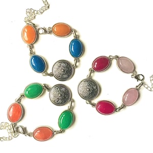 Puede incluir: Tres pulseras con piedras ovaladas de colores y detalles metálicos ornamentados. Las pulseras están hechas de metal dorado y presentan una variedad de colores, incluyendo rosa, verde, azul y naranja.