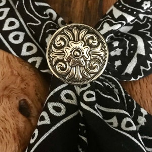 May include: A silver-toned metal bandana clasp with a floral design. The clasp is on a black and white bandana.
