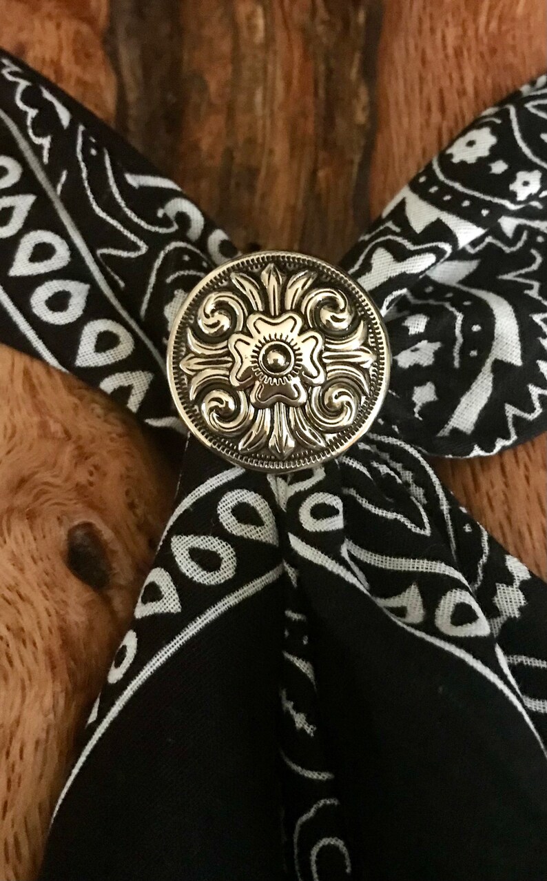 May include: A silver-toned metal bandana clasp with a floral design. The clasp is on a black and white bandana.