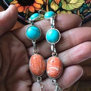 May include: Two silver bracelets with turquoise and orange stones. The bracelets have a chain link closure.