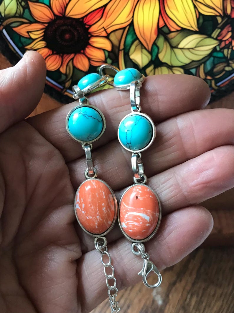 May include: Two silver bracelets with turquoise and orange stones. The bracelets have a chain link closure.