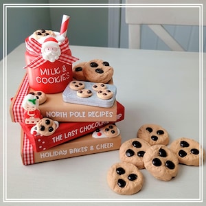 May include: A decorative stack of three books titled North Pole Recipes, The Last Chocolate, and Holiday Bakes & Cheer, topped with a red jar labeled Milk & Cookies, a Santa ornament, a striped straw, and miniature chocolate chip cookies.