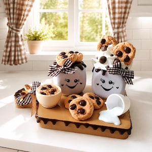 May include: A whimsical kitchen scene featuring decorative cookie-themed items. Includes two smiling face jars with cookies, a small bowl, and a tray with cookies and a spilled milk cup. Accented with black and white checkered bows and chocolate drizzle.