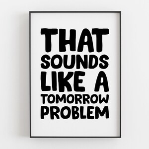 May include: A framed print featuring the phrase "THAT SOUNDS LIKE A TOMORROW PROBLEM" in bold, black lettering. The text is set against a white backdrop, enclosed within a black frame.