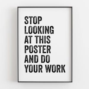 May include: A rectangular wall poster in a thin black frame featuring bold, black, distressed-texture sans-serif capital letters on a white background that read: STOP LOOKING AT THIS POSTER AND DO YOUR WORK. The text is centred and vertically aligned.