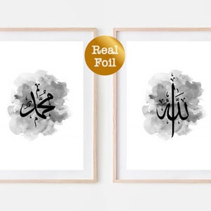 Puede incluir: Dos impresiones enmarcadas con fondos de acuarela en blanco y negro. Las impresiones presentan caligrafía árabe en negro, una que dice "Allah" y la otra que dice "Muhammad".