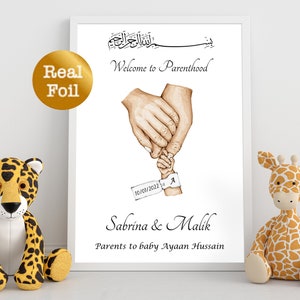 Op de afbeelding: Een witte ingelijste print met een aquarel-illustratie van twee handen die de hand van een baby vasthouden. De tekst luidt "Welkom in het ouderschap" en bevat de datum "10/07/2022" en de namen "Sabrina & Malik" en "Ouders van baby Ayaan Hussain".