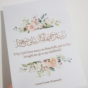 May include: A white card with a floral design and a gold Arabic inscription. The text below the inscription reads 'O My Lord! Have mercy on them both, just as they brought me up in my childhood.' The card is signed 'Love From Bismah'.