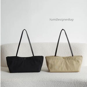 May include: Two rectangular tote bags, one black and one beige, each featuring long black shoulder straps and a single center snap button closure. The text YumiDesignerBag is visible in the upper right corner of the image.