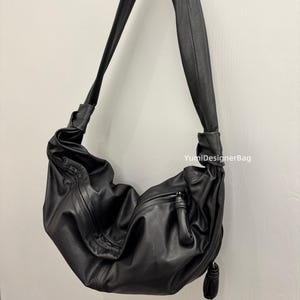 May include: A black leather shoulder bag with a long strap. The bag has a slouchy design with a zipper closure and a tassel detail. The text "YumiDesignerBag" is visible on the right side of the bag.
