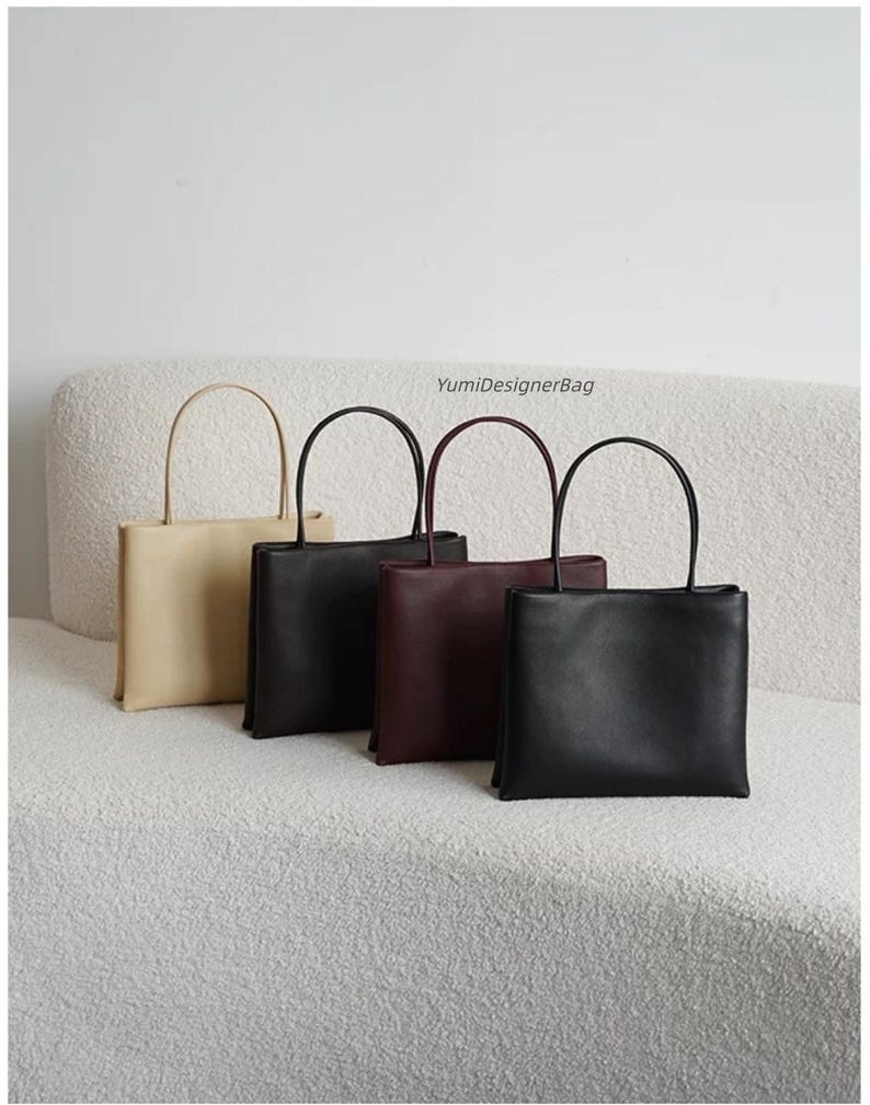 May include: Four rectangular handbags with thin top handles, arranged in a row. The bags are colored beige, black, dark brown, and black. Each bag features a smooth finish and a structured shape. The text YumiDesignerBag is visible above them.