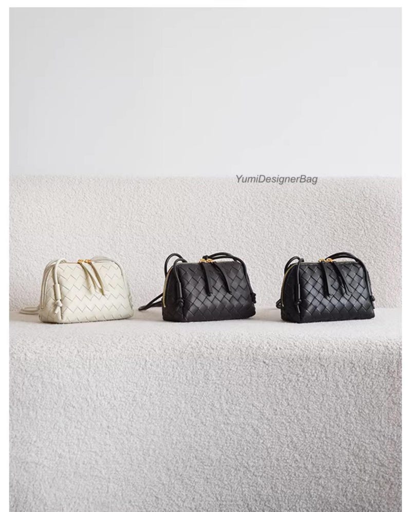 K&ouml;nnte beinhalten: Drei geflochtene Leder-Umh&auml;ngetaschen in Creme, Schwarz und Schwarz werden auf einer strukturierten wei&szlig;en Oberfl&auml;che pr&auml;sentiert. Jede Tasche hat einen Rei&szlig;verschluss oben, einen kleinen Griff und einen goldfarbenen Rei&szlig;verschluss. Die Taschen sind von YumiDesignerBag.