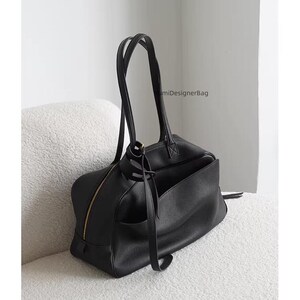 May include: Black leather tote bag with a gold zipper and handles. The bag has an exterior pocket and is sitting on a white, textured surface. The bag has the text "miDesignerBag".