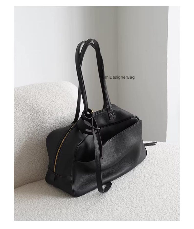 May include: Black leather tote bag with a gold zipper and handles. The bag has an exterior pocket and is sitting on a white, textured surface. The bag has the text "miDesignerBag".