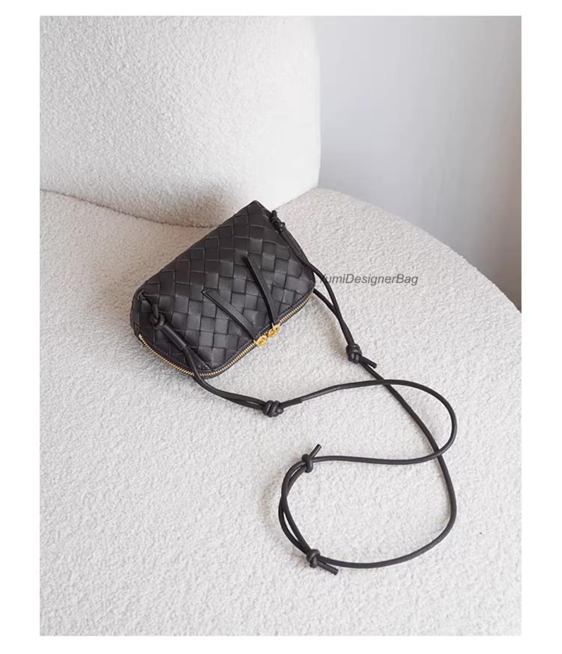 K&ouml;nnte beinhalten: Schwarze Crossbody-Tasche aus geflochtenem Leder mit goldenem Rei&szlig;verschluss und Riemen. Die Tasche hat eine rechteckige Form mit abgerundeten Kanten. Der Riemen ist d&uuml;nn und verstellbar. Die Tasche liegt auf einer wei&szlig;en Oberfl&auml;che.