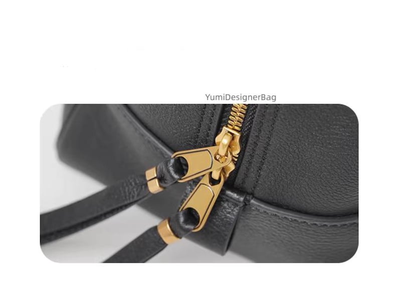 May include: Close-up of a black leather bag with a gold zipper and matching gold zipper pulls. The bag has a strap and the text "YumiDesignerBag" is visible.