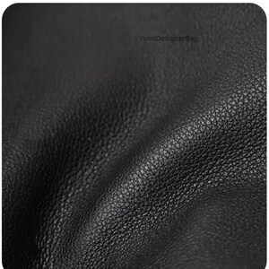 May include: Close-up of a black leather material with a textured surface. The leather has a natural grain and a matte finish. The image shows the details of the leather's texture and color.