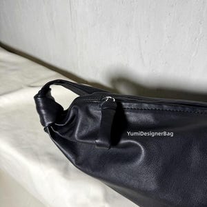 May include: Black leather shoulder bag with a knotted handle. The bag features a zipper closure and a smooth, textured surface. The brand name "YumiDesignerBag" is visible on the side of the bag.
