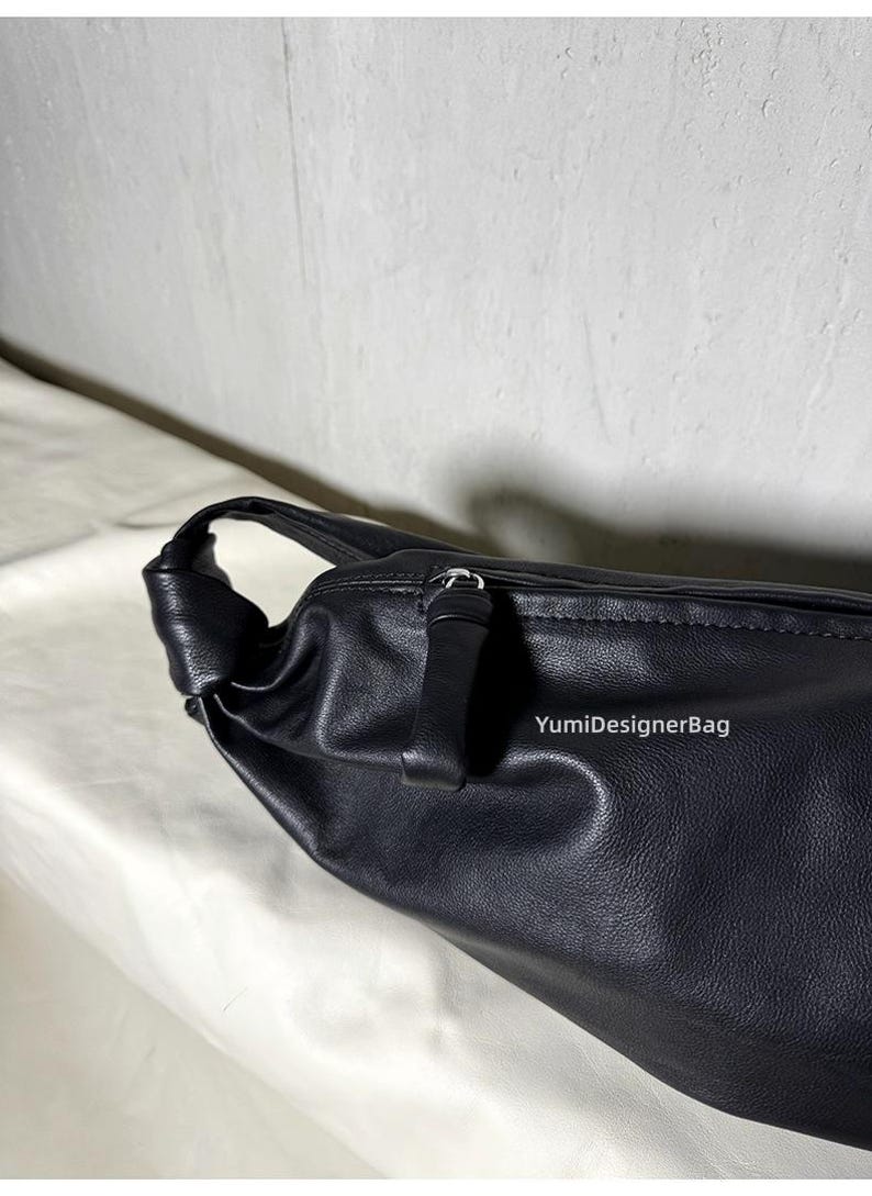 May include: Black leather shoulder bag with a knotted handle. The bag features a zipper closure and a smooth, textured surface. The brand name "YumiDesignerBag" is visible on the side of the bag.