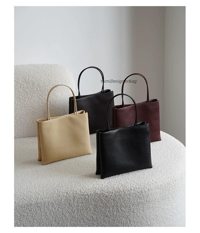 May include: Four rectangular handbags with thin top handles, featuring the text YumiDesignerBag. The bags are available in beige, black, and dark red, each with a smooth finish and a structured, upright design with a flat base and clean lines.