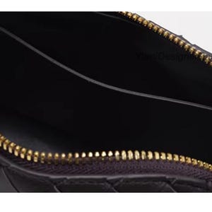 K&ouml;nnte beinhalten: Nahaufnahme einer schwarzen Leder-Clutch mit einem gewebten Muster. Der Innenraum ist dunkel, und der goldene Rei&szlig;verschluss ist ge&ouml;ffnet, wodurch das Innere sichtbar wird. Ein stilvolles Accessoire.