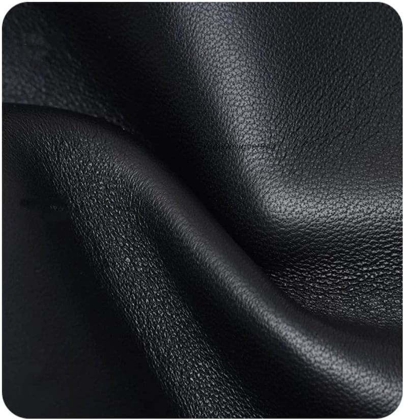 May include: A close-up view of black leather material featuring a distinct pebbled texture. The surface shows natural folds and soft curves, highlighting the matte finish and the irregular grain pattern characteristic of the hide's organic surface.