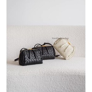 K&ouml;nnte beinhalten: Drei gewebte Leder-Umh&auml;ngetaschen in Schwarz, Creme und Dunkelbraun werden auf einer strukturierten wei&szlig;en Oberfl&auml;che pr&auml;sentiert. Jede Tasche verf&uuml;gt &uuml;ber einen Rei&szlig;verschluss mit goldfarbener Hardware und d&uuml;nnen Schulterriemen. Die Taschen sind l&auml;ssig und stilvoll angeordnet.