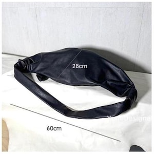 May include: Black shoulder bag with a soft, gathered design. The bag is approximately 28cm wide and 60cm long. The bag has a long strap and is made of a smooth material. The bag is shown on a white surface.