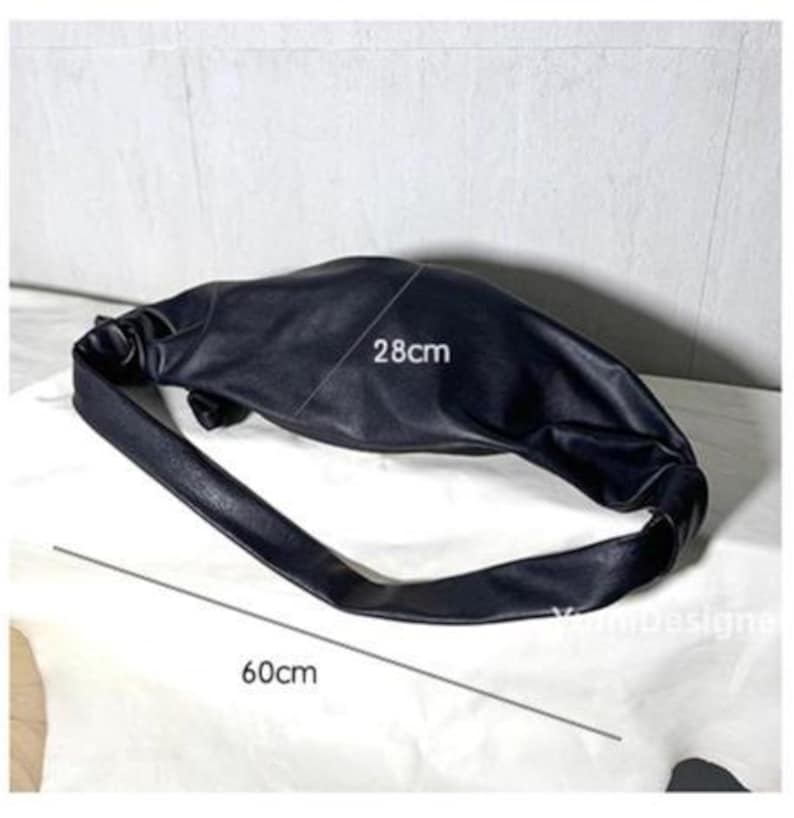 May include: Black shoulder bag with a soft, gathered design. The bag is approximately 28cm wide and 60cm long. The bag has a long strap and is made of a smooth material. The bag is shown on a white surface.