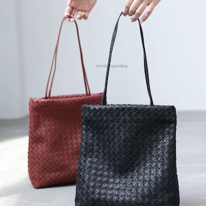Puede incluir: Dos bolsos tote rectangulares con textura trenzada, uno negro y otro rojo oscuro. Cada bolso cuenta con correas finas para el hombro y el texto YumiDesignerBag impreso en letras pequeñas de color gris entre ambos bolsos.
