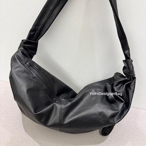 May include: A black leather shoulder bag with a knotted strap. The bag has a curved shape and a zipper closure. The text "YumiDesignerBag" is visible on the side of the bag.