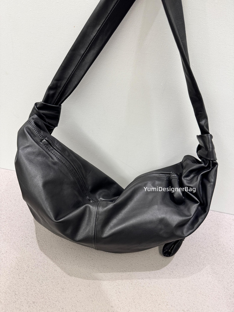 May include: A black leather shoulder bag with a knotted strap. The bag has a curved shape and a zipper closure. The text "YumiDesignerBag" is visible on the side of the bag.