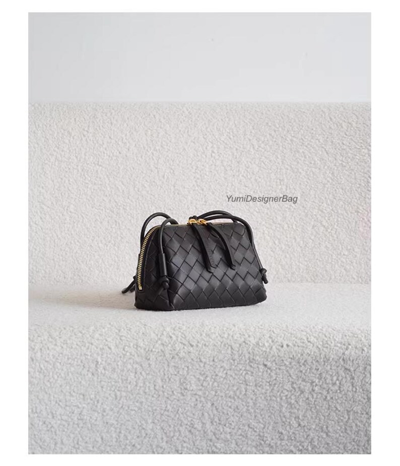 K&ouml;nnte beinhalten: Schwarze Handtasche aus geflochtenem Leder mit goldenem Rei&szlig;verschluss und Griffen. Die Tasche hat eine rechteckige Form und ein geflochtenes Muster. Der Text "YumiDesignerBag" ist im Hintergrund sichtbar.