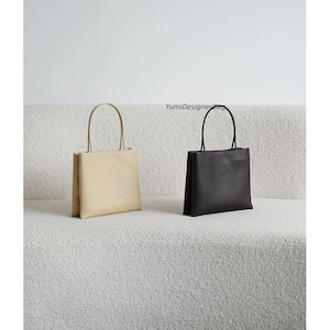 May include: Two rectangular tote bags with thin handles, one in beige and one in black, featuring a smooth finish and a structured silhouette. The text YumiDesignerBag is visible in the center above the black bag.
